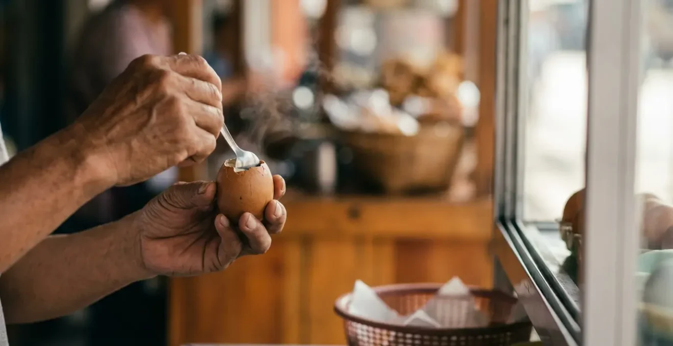 Close-up of hands carefully peeling the top of a balut egg to preserve the broth inside