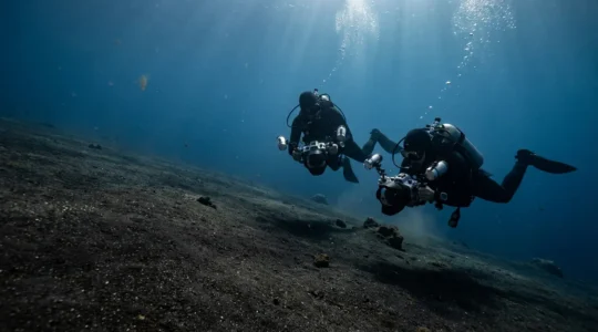 Underwater macro photographers examining tiny creatures on volcanic black sand bottom
